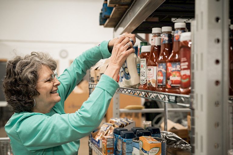 A woman arranges bottles on a shelf.